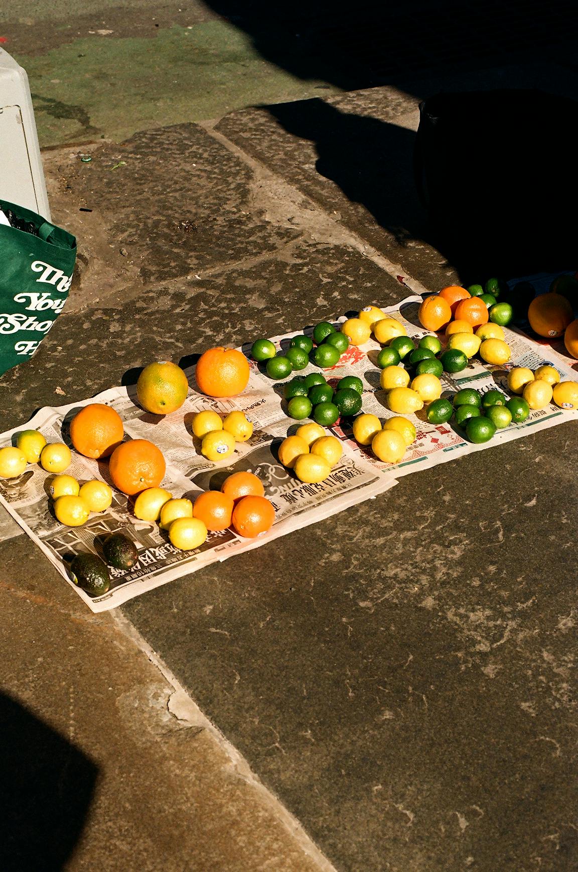 A display of various citrus resting on newspaper on the ground.